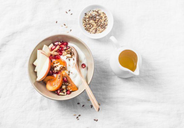 Full fruit and greek yogurt breakfast bowl. Persimmon, apple, walnuts, pomegranates and natural yogurt. Healthy food concept on light background, top view. (Shutterstock)