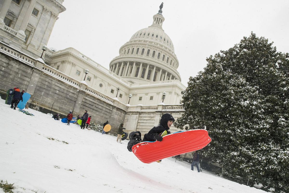 Two children go over a ramp as they sled on Capitol Hill as a winter storm arrives in the region, Sunday, Jan. 13, 2019, in Washington. (AP Photo/Alex Brandon)