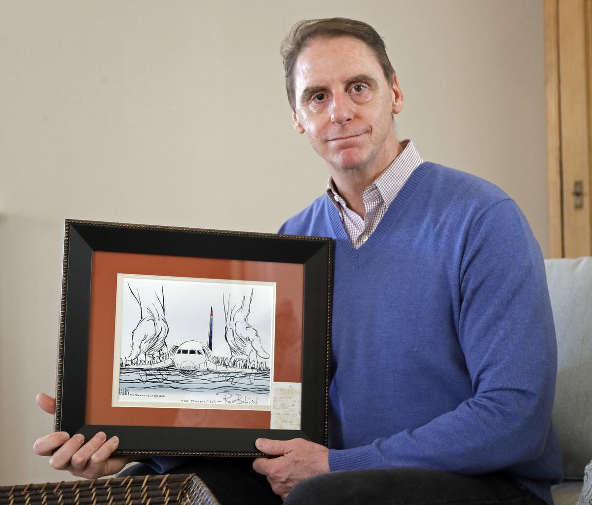 In this Jan. 10, 2019 photo, Steve O'Brien poses for a photo at his home in Charlotte, N.C., with an editorial cartoon framed with his boarding pass from US Airways Flight 1549, that eventually crash-landed in the Hudson River on Jan. 19, 2009. Tuesday, Jan. 19, 2019 is the 10th anniversary of the flight known as the "Miracle on the Hudson" after all 155 passengers and crew members survived. (Chuck Burton/AP Photo)