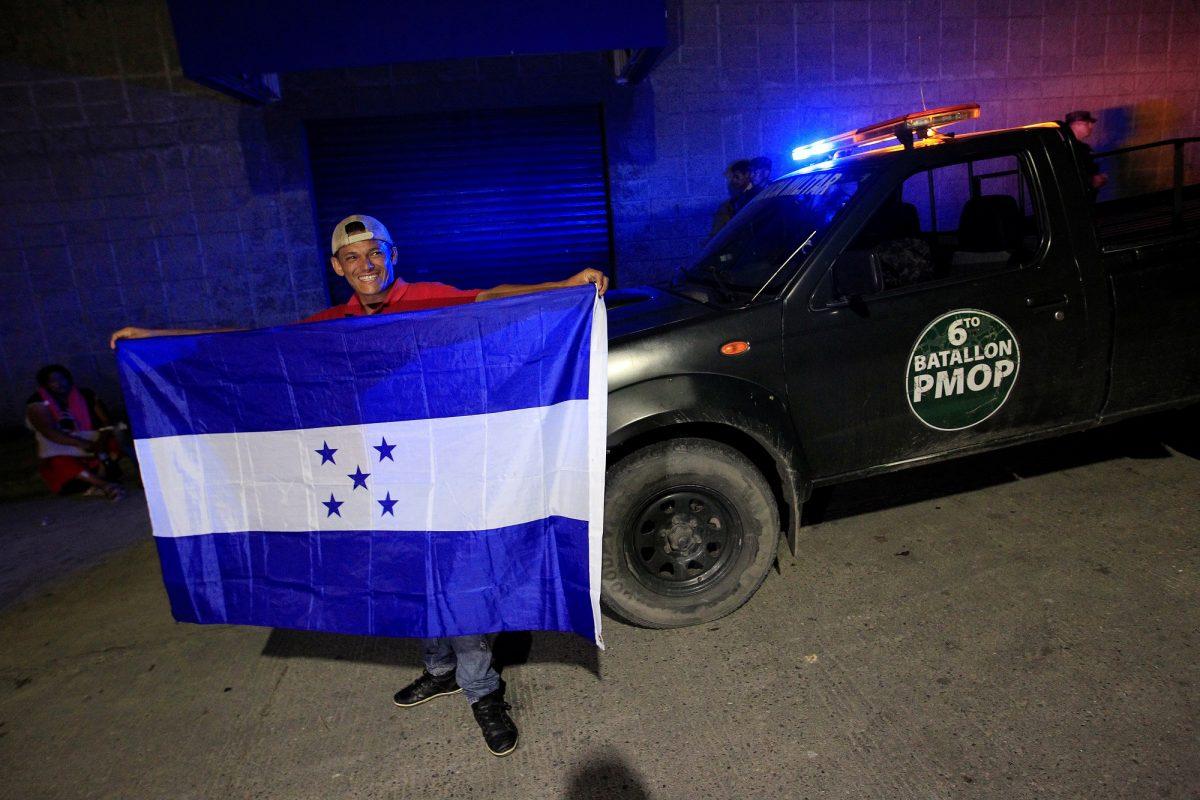 A man holds a flag of Honduras at a bus station in San Pedro Sula in front of a military vehicle before leaving with a new caravan of migrants to the United States on Jan. 14, 2019. (Jorge Cabrera/Reuters)