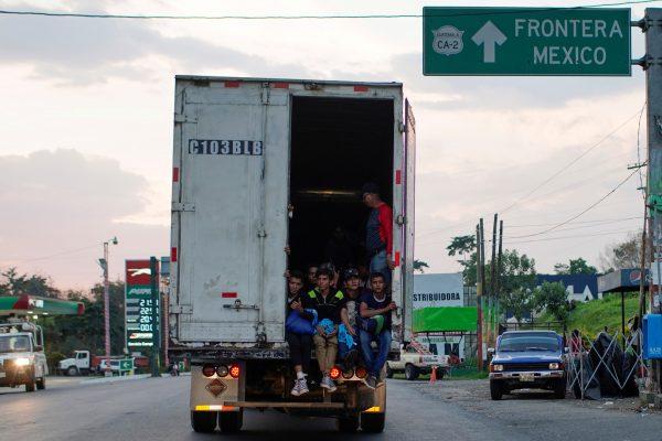 Immigrants pass by a highway sign that reads in Spanish: "Mexico Border", as they take a lift in the back of a truck during their journey towards the United States, in Pajapita, Guatemala, on Jan. 17, 2019. (Alexandre Meneghini/Reuters)