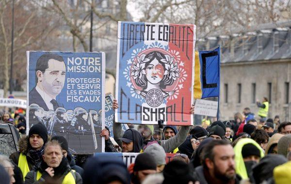 Protesters wearing yellow vests take part in a demonstration by the "yellow vests" movement. The signs read "Our Mission. Protect and Serve Tax Evaders" and "Liberty, Equality, Flashball."<br/>in Paris, France, on Jan. 19, 2019. (Charles Platiau/Reuters)