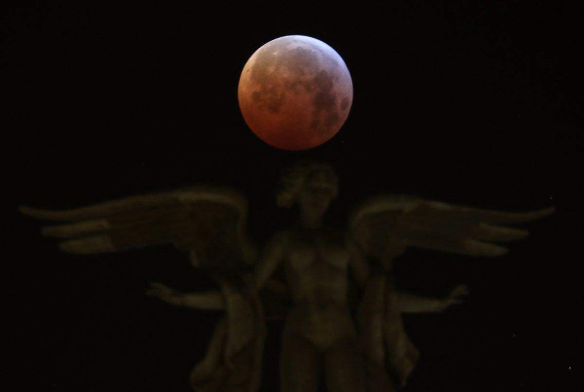 The moon is seen over "Victoria Alada" statue on the top of Metropoli building during a total lunar eclipse, known as the "Super Blood Wolf Moon" in Madrid, Spain, on Jan. 21, 2019. (Sergio Perez/Reuters)