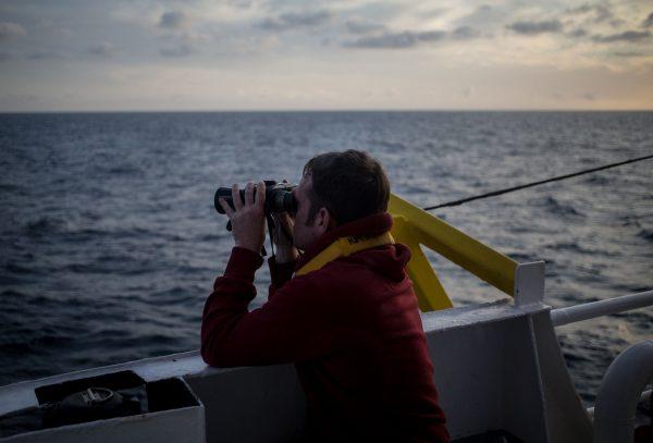 One of the crew members of the Dutch-flagged rescue vessel Sea Watch 3 keeps a watch on the sea with binoculars during a rescue operation off Libya's coasts on January 18, 2019. (Federico Scoppa/AFP/Getty Images)