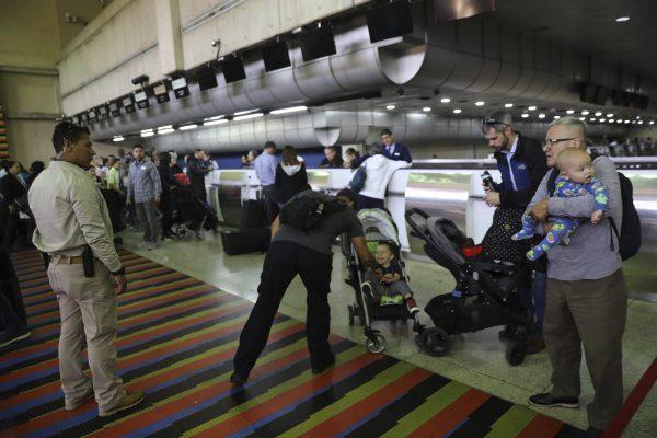 U.S. embassy employees and their family members, two men and children at right, prepare to depart Simon Bolivar international airport as two security officers, left, stand by, in La Guaira, Venezuela, on Jan. 25, 2019. (Rodrigo Abd/AP Photo)