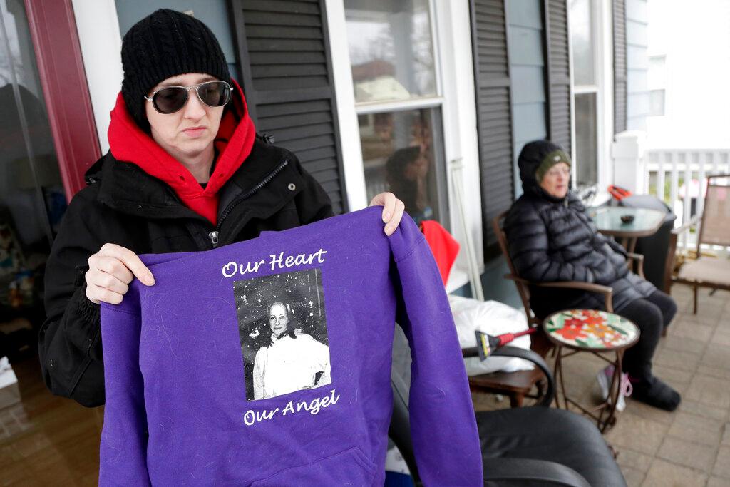 In a photo taken Friday, Jan. 18, 2019, Barbara Fuller, left, holds a sweatshirt honoring her late sister, Sarah Fuller, as their mother Deborah Fuller, right, looks on from their porch in West Berlin, N.J. The trial of the Insys Therapeutics Inc. founder John Kapoor, who accused of scheming to bribe doctors into prescribing a powerful painkiller, is putting a spotlight on the nation's deadly opioid crisis. (AP Photo/Julio Cortez)