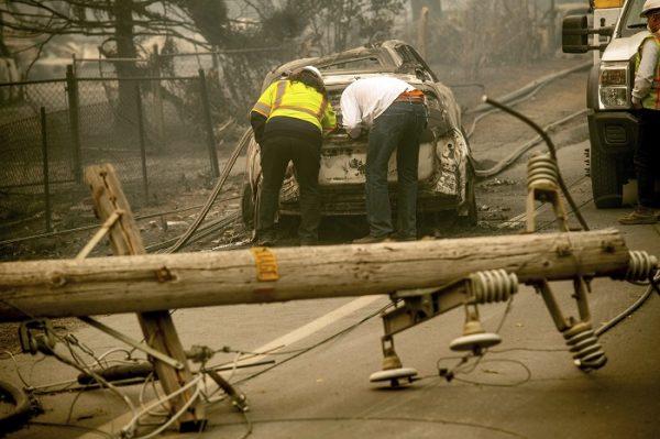 A downed power utility pole in the foreground, Eric England, right, searches through a friend's vehicle after the wildfire burned through Paradise, Calif., on Nov. 10, 2018. (Noah Berger/AP Photo, File)