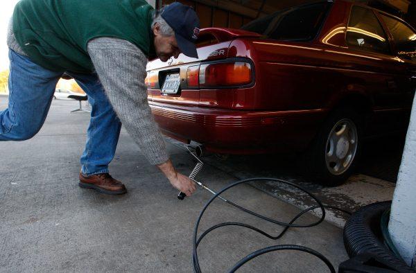 Alex Gromov puts a probe into the tailpipe of a car as he performs a smog check at Marinwood Smog Check in San Rafael, California on December 12, 2007. (Photo by Justin Sullivan/Getty Images)