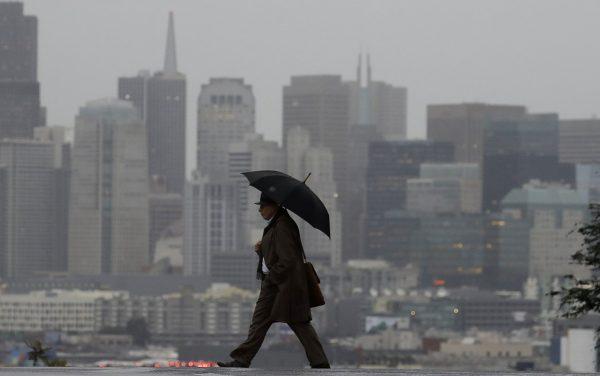 A man carries an umbrella as he crosses the street with the skyline at the rear in San Francisco, on Feb. 1, 2019. (Jeff Chiu/AP Photo)