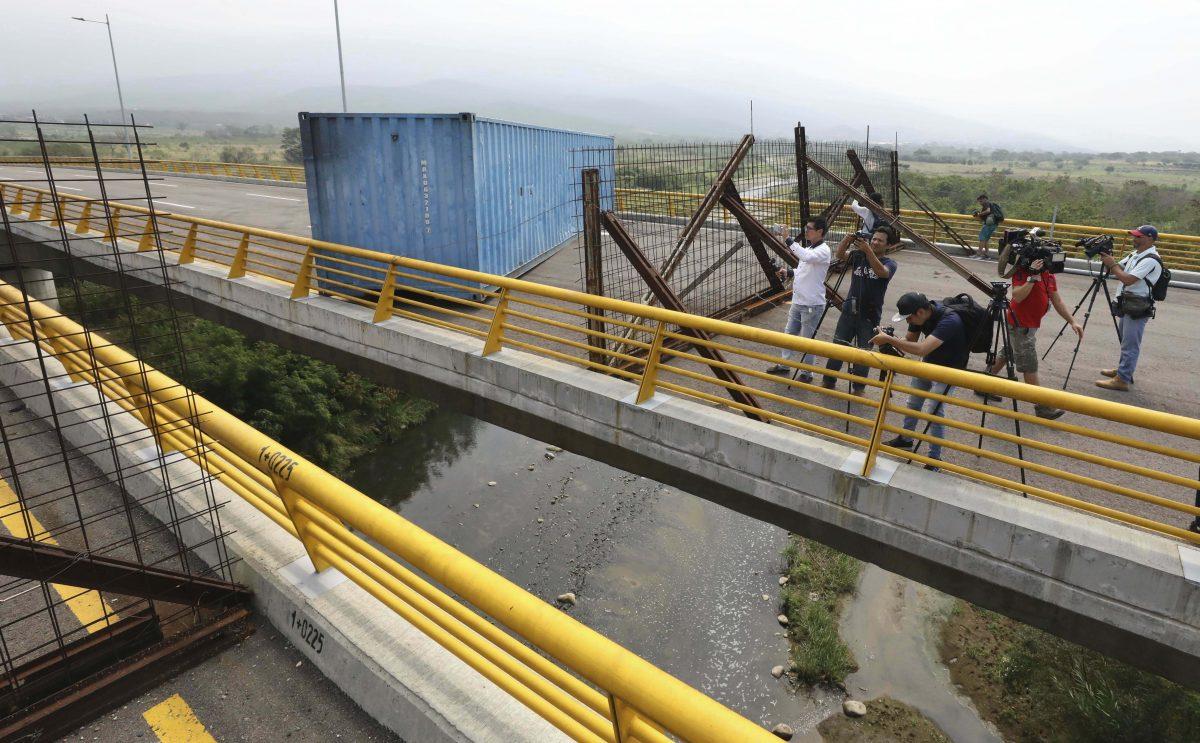 Journalists record a fuel tanker, cargo trailers, and makeshift fencing, used as barricades by Venezuelan authorities attempting to block humanitarian aid entering from Colombia on the Tienditas International Bridge that links the two countries as seen from the outskirts of Cucuta, Colombia, on Feb. 6, 2019. (AP Photo/Fernando Vergara)