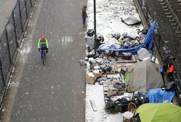 A bicyclist rides past a homeless encampment as snow falls in Seattle, on Feb. 8, 2019. (Elaine Thompson/AP Photo)