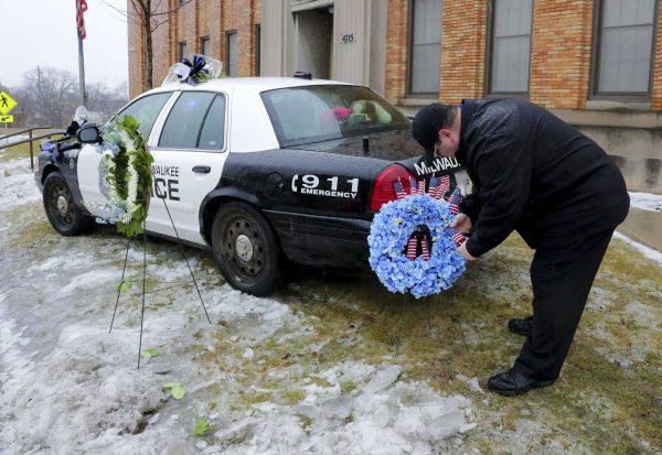 Timothy Nelson, of Oak Creek, Wis., places small flags in a bouquet near a squad car adorned with flowers as a memorial for fallen Milwaukee Police Officer Matthew Rittner at the Neighborhood Task Force police building in Milwaukee, on Feb. 7, 2019. (Mike De Sisti/Milwaukee Journal-Sentinel via AP)