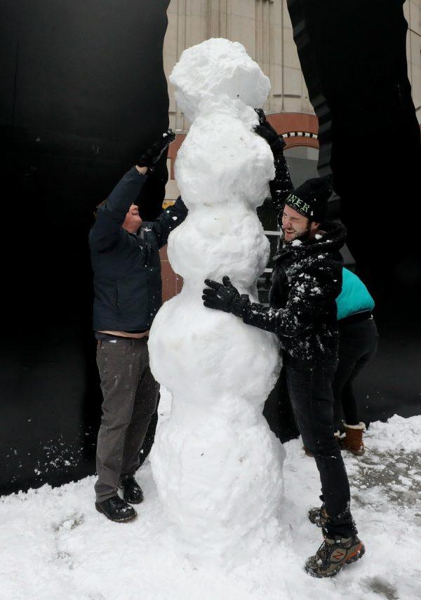 It's a tall order as Michael Delbridge (L), Dre Spliffman, and three other friends gather more snow to construct a snowman beneath Hammering Man in front of the Seattle Art Museum in Washington, on Feb 9, 2019. (Alan Berner/The Seattle Times via AP)