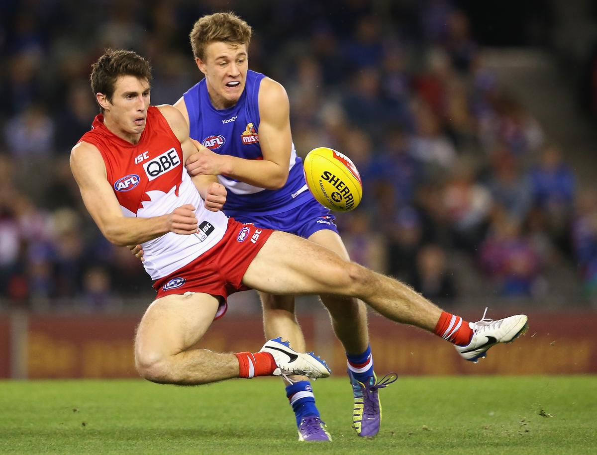 Dean Towers of the Swans handballs whilst being tackled by Jackson Macrae of the Bulldogs during the round 22 AFL match between the Western Bulldogs and the Sydney Swans at Etihad Stadium on Aug. 24, 2014 in Melbourne, Australia. (Quinn Rooney/Getty Images)