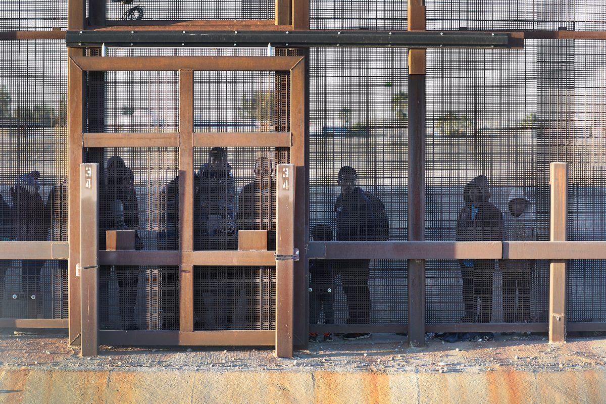 Migrants stand together along the U.S./Mexican border wall as they wait to turn themselves over to the U.S. Border Patrol in El Paso, Texas, on Feb. 12, 2019. (Joe Raedle/Getty Images)