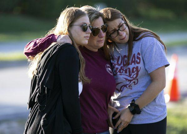 (L-R) Emma Rothenberg, her mother Cheryl Rothenberg and sister, Marjory Stoneman Douglas High School student Sophia Rothenberg embrace at a memorial marking the anniversary of a mass shooting at the school in Parkland, Fla., on Feb. 14, 2019. (Al Diaz/Miami Herald via AP)