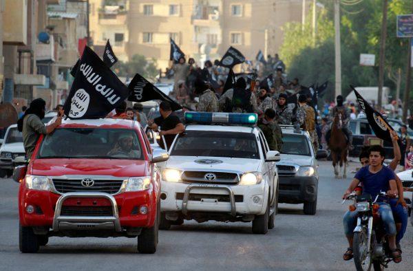 ISIS terrorists waving flags travel in vehicles as they take part in a military parade along the streets of Syria's northern Raqqa province, on June 30, 2014. (Stringer/Reuters)