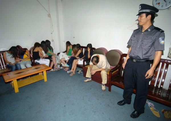 A policeman guards arrested prostitutes and a whoremaster at an entertainment center in Guangzhou, Guangdong Province, China on Oct. 18, 2005. Prostitutes were the focus of the Ministry of Health's attempt to stem the spread of HIV/AIDS. (China Photos/Getty Images)
