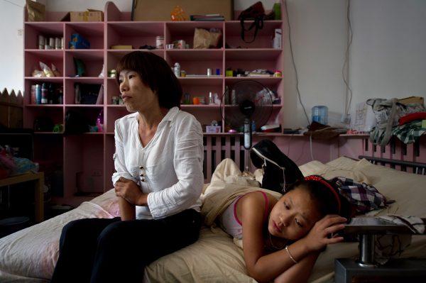 HIV carrier Liu Ximei (L) looking on as her friend Tao Jing Lan (R), also HIV positive, rests on a bed during a visit to Beijing on Aug. 2, 2012. Ximei contracted the HIV virus after blood sellers at a rural hospital injected her with a used needle following a severe accident as a young girl in which her hair was caught in farm machinery, tearing away her scalp. (Ed JonesAFP/GettyImages)