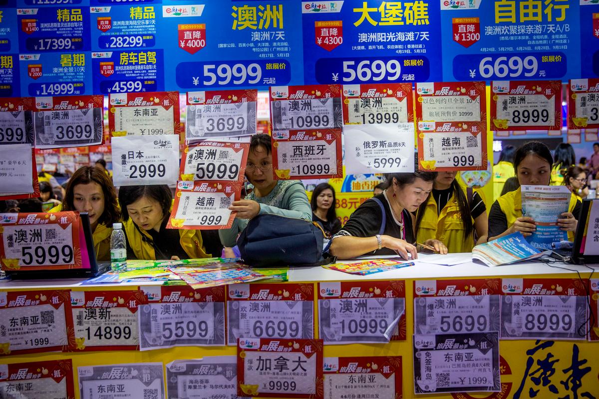 People check on travel packages offered by travel agencies during the Guangzhou International Travel Fair in Guangzhou in south China's Guangdong Province on March 3, 2018. Travelers in China were blocked from buying plane tickets 17.5 million times in 2018 as a penalty for failing to pay fines or other offenses, the Chinese regime reported that week on penalties imposed under a controversial "social credit" system. (Chinatopix via AP)