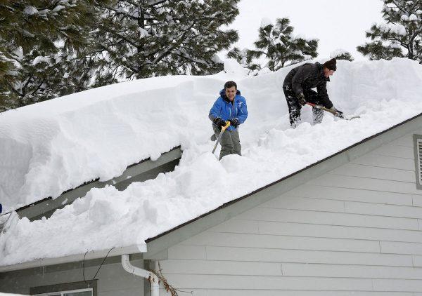 Homeowner Kevin Ireland, right, and Tommy Tokarczyk clear several feet of snow off the roof in the Durango West I Subdivision on Feb. 22 2019. (Jerry McBride/The Durango Herald via AP)