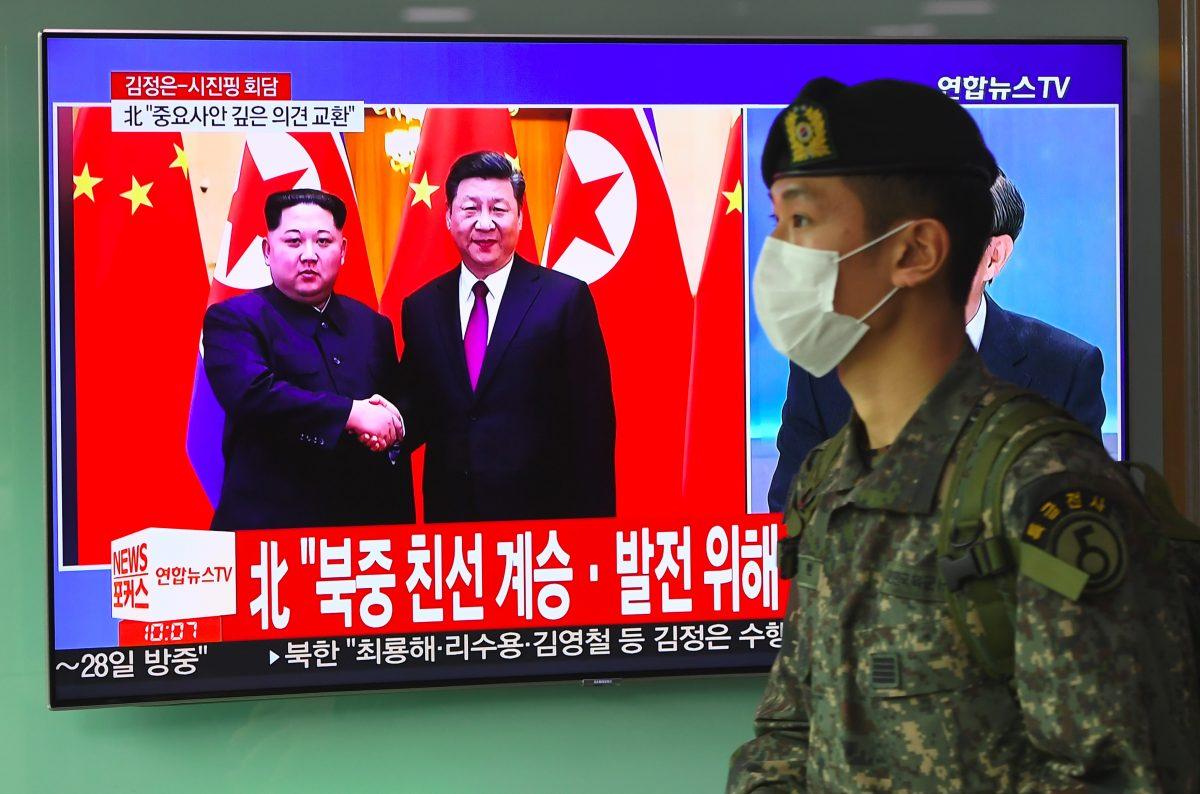 A South Korean soldier walks past a television news screen reporting about a visit to China by North Korean leader Kim Jong Un, pictured with Chinese leader Xi Jinping, at a railway station in Seoul on March 28, 2018. (JUNG YEON-JE/AFP/Getty Images)