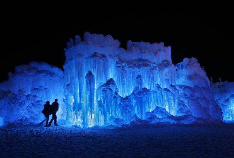 A couple heads toward an entrance to a cavern at Ice Castles in North Woodstock, N.H., on Jan. 26 2019.  A team starts building massive walls in December to create a spectacular winter experience. (Robert F. Bukaty/AP Photo)