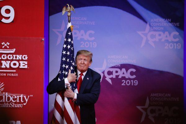 President Donald Trump hugs the American flag as he comes on stage at the CPAC convention in Maryland on March 2, 2019. (Samira Bouaou/The Epoch Times)