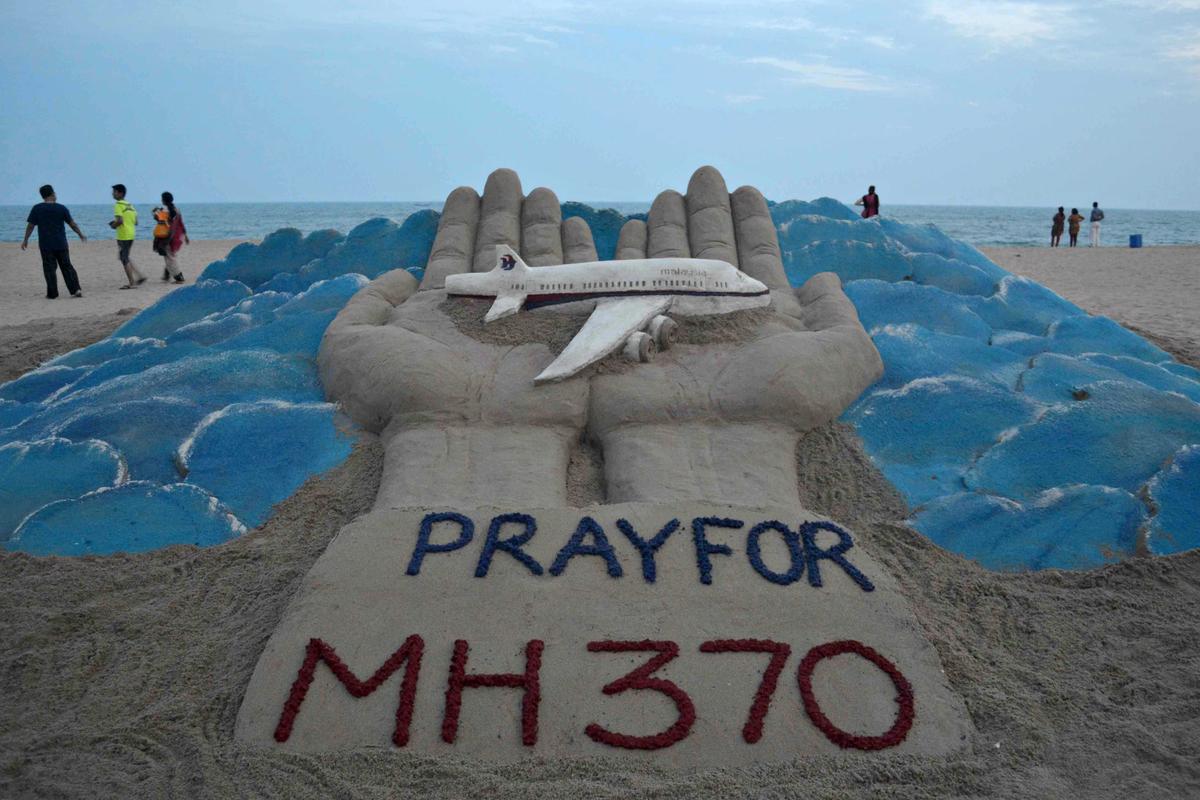 Beachgoers walk past a sand sculpture made by Indian sand artist Sudersan Pattnaik with a message of prayers for the missing Malaysian Airlines flight MH370. (ASIT KUMAR/AFP/Getty Images)