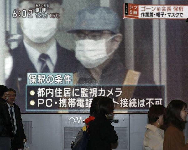 People walk by a monitor which reports on the bail of former chairman of Nissan Motor Co., Carlos Ghosn, in Osaka, western Japan, on March 6, 2019. (Kyodo News via AP)