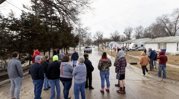 A crowd gathers to watch residents make their way in and out of a flooded neighborhood on March 17, 2019, in Omaha, Neb. Hundreds of people were evacuated from their homes in Nebraska and Iowa as levees succumbed to the rush of water. (Kent Sievers/Omaha World-Herald via AP)