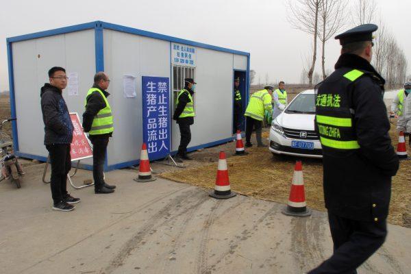 Police officers and workers in protective suits are seen at a checkpoint on a road leading to a farm owned by Hebei Dawu Group where African swine fever was detected, in Xushui district of Baoding, Hebei Province, China on Feb. 26, 2019. (Hallie Gu/Reuters)
