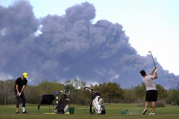 Golfers practice at the Battleground Golf Course driving range as a chemical fire at Intercontinental Terminals Company continues to send dark smoke over Deer Park, Texas, on March 19, 2019. (Melissa Phillip/Houston Chronicle via AP)