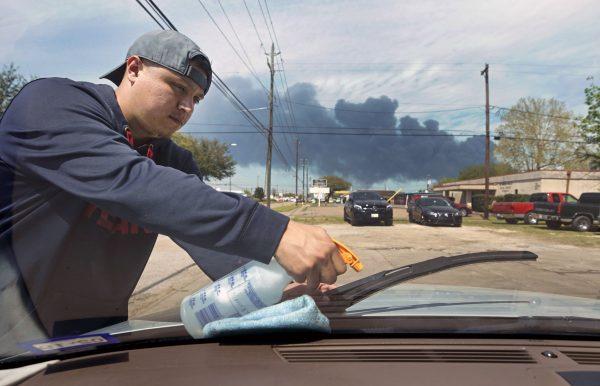 Carlos Razo is shown through the windshield as he cleans a car at Juan's Hand Carwash, 1905 Center St., as the chemical fire at Intercontinental Terminals Company continues to send dark smoke over Deer Park, Texas, on March 19, 2019. (Melissa Phillip/Houston Chronicle via AP)