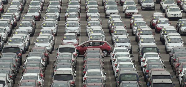 A man drives a red car past a parking lot where large numbers of newly manufactured cars are parked at Dayaowan port of Dalian, Liaoning Province on June 10, 2012. (Reuters)