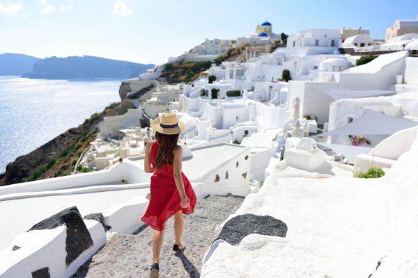 Tourist woman visiting the famous white village with the mediterranean sea and blue domes. Europe summer destination. (Shutterstock)