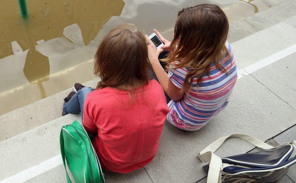 Two girls sit and discuss apps on their phones. (Sean Gallup/Getty Images)