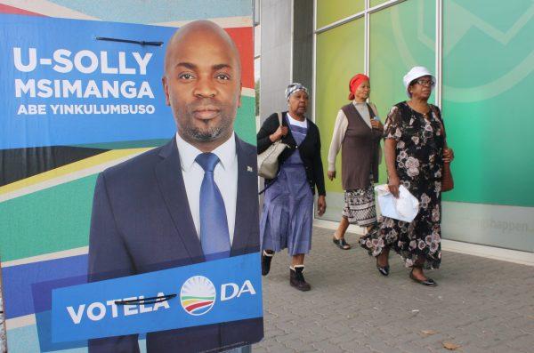 Women walk past a poster urging citizens to vote for a candidate of the opposition Democratic Alliance in Krugersdorp, South Africa. (Darren Taylor for The Epoch Times)