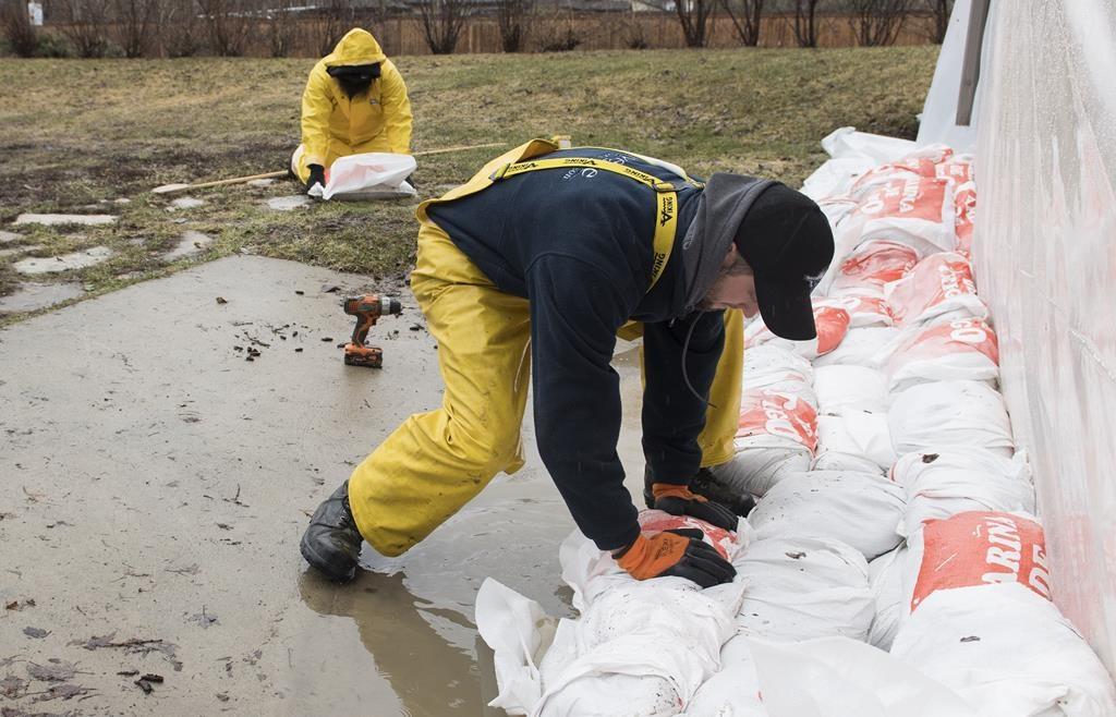 A man places a sandbag next to the foundation of a house in the town of Hudson, Que. west of Montreal, on April 19, 2019. (The Canadian Press/Graham Hughes)