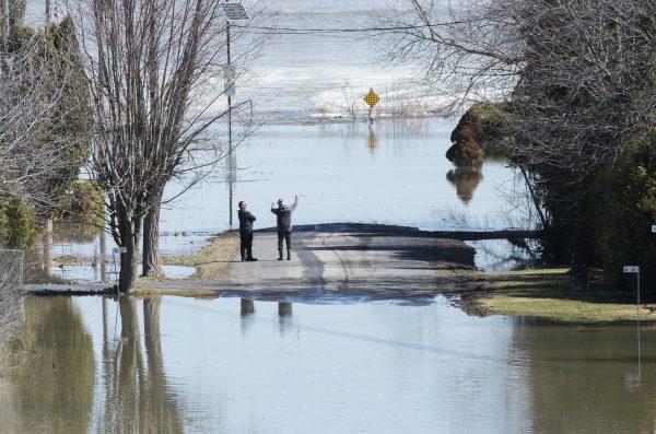 Two men look out towards the Ottawa River on a residential street surrounded by floodwaters in the town of Rigaud, Que., on April 22, 2019. (The Canadian Press/Graham Hughes)