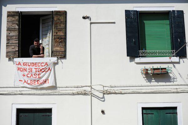 Alessandro Dus, 34, talks on the phone in his illegally occupied apartment in the Casette neighborhood in Venice, Italy, April 3, 2019. The banner reads "Don't touch the Giudecca. More houses, less hotels". (Guglielmo Mangiapane/Reuters)
