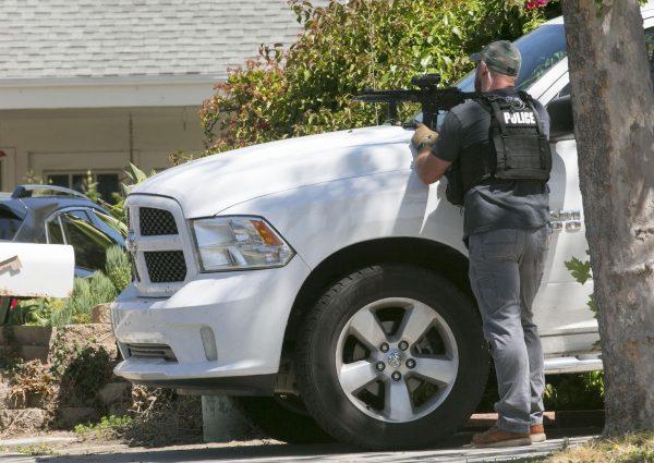 A San Diego Police officer keeps aim on the house thought to be the home of 19 year-old John T. Earnest, who is a suspect in the shooting of several people in a Poway synagogue in San Diego, Calif., on April 27, 2019. (John Gibbins/The San Diego Union-Tribune via AP)
