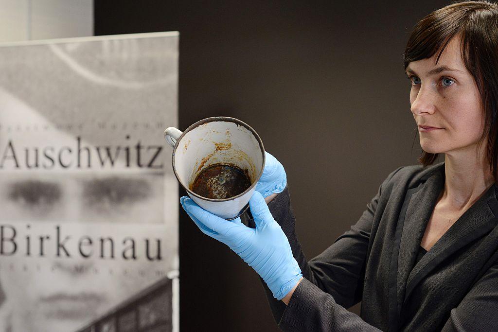 A woman presents a metal mug with a double bottom in which a gold ring and necklace were found by employees of the Auschwitz-Birkenau museum in Oswiecim, Poland. (©Getty Images | <a href="https://www.gettyimages.com/detail/news-photo/woman-presents-on-may-19-2016-a-metal-mug-with-a-double-news-photo/532588108">BARTOSZ SIEDLIK</a>)