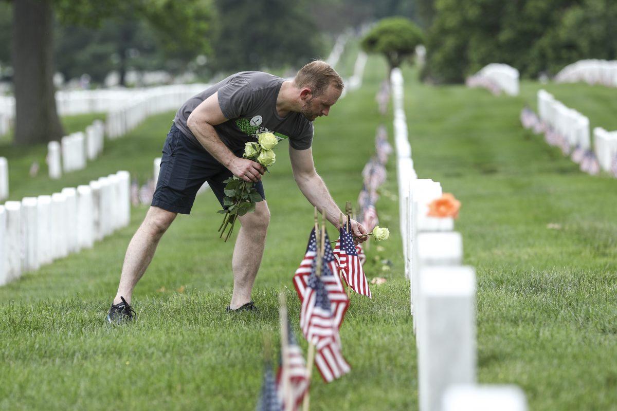 A volunteer places flowers at tombstones in Arlington Cemetery in Arlington, Va., on May 26, 2019. (Samira Bouaou/The Epoch Times)