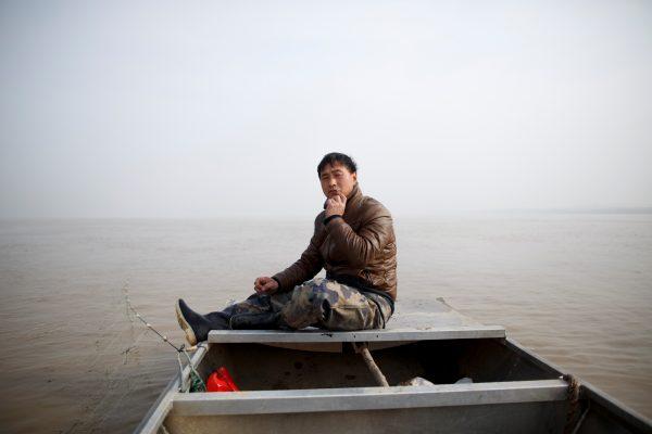 Fisherman Sun Lianxi sits in his boat as he travels down the Yellow River to cast his net on the northern outskirts of Zhengzhou, Henan Province, China on Feb. 21, 2019. (Thomas Peter/Reuters)