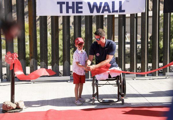 Benton Stevens, 7, and Brian Kolfage, founder of We Build the Wall, cut the ribbon at the official ceremony for the new half-mile section of border fence built from donations, at Sunland Park, N.M., on May 30, 2019. (Charlotte Cuthbertson/The Epoch Times)