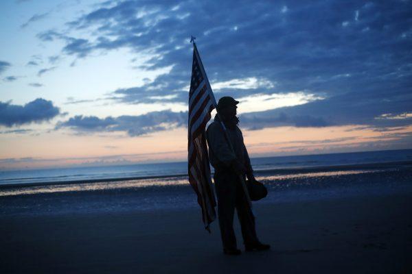 Udo Hartung from Frankfurt, Germany, a World War II reenactor, holds the U.S. flag as he stands at dawn on Omaha Beach, in Normandy, France on June 6, 2019, during commemorations of the 75th anniversary of D-Day. (Thibault Camus/Photo/AP)