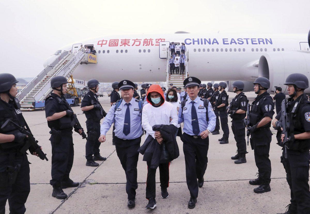 Police escort criminal suspects as they get off a plane at Beijing Capital International Airport in Beijing on June 7, 2019. A group of 94 Taiwanese accused of telephone and online fraud arrived at Beijing airport after being extradited from Spain. (Yin Gang/Xinhua via AP)