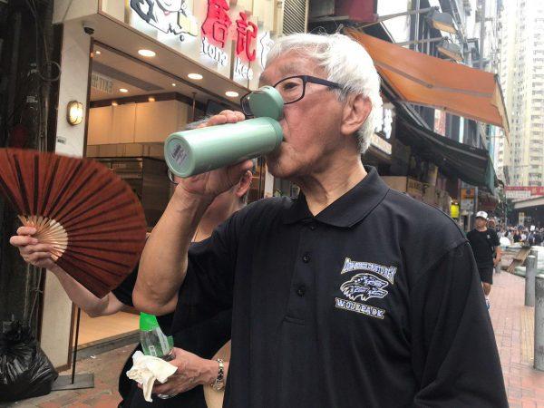 Cardinal Joseph Zen takes a sip of water while taking part in the anti-extradition bill march in Hong Kong on June 16, 2019. (Lin Yi/The Epoch Times)