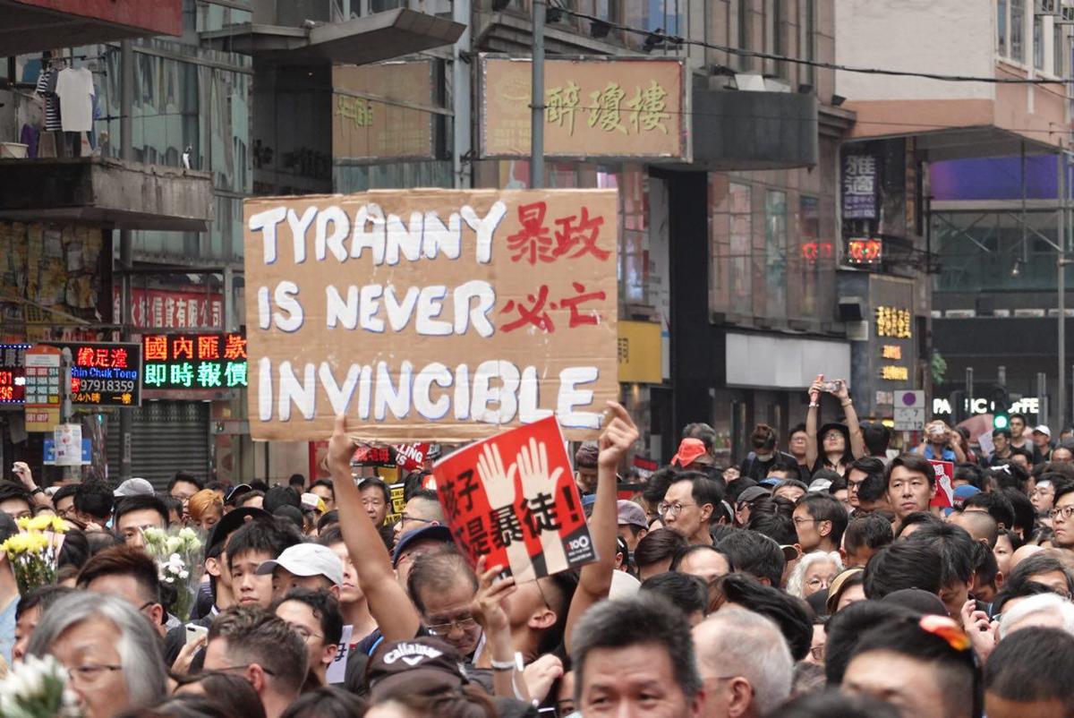 One protester holds up a sign that reads “Tyranny Is Never Invincible,” in a reference to the Hong Kong government under leader Carrie Lam on June 16, 2019. Another protester holds up a sign in red, with the Chinese characters “Children Are Not Rioters.” (Yu Gang/The Epoch Times)